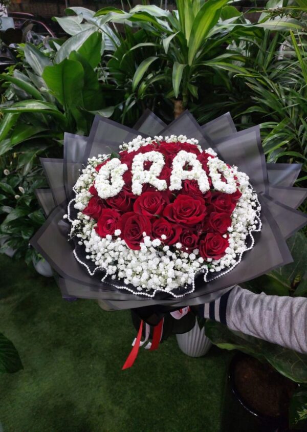 Graduation bouquet of red roses with 'GRAD' lettering in white flowers, wrapped in black paper, perfect for graduation gifts in Dubai.