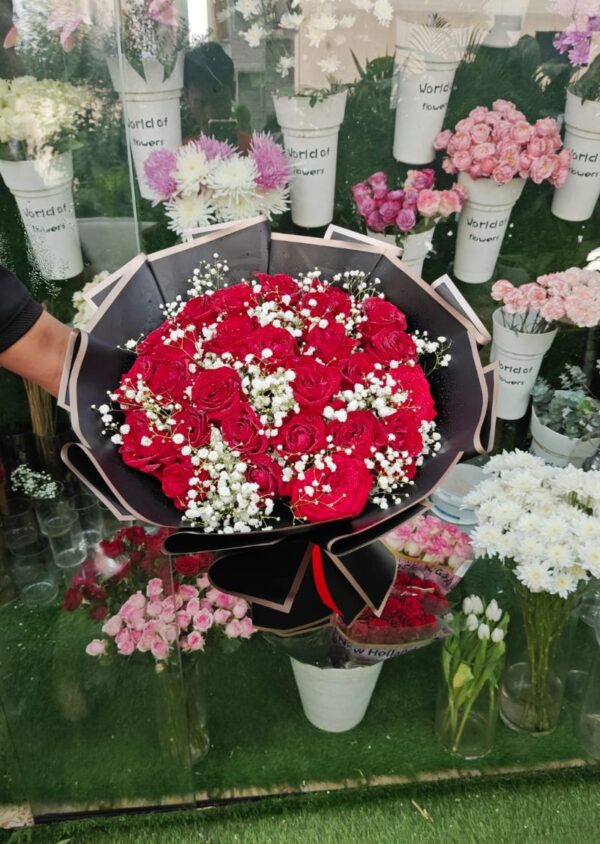 Elegant bouquet of fresh red roses and baby’s breath wrapped in black paper with ribbon – romantic floral gift for anniversary or Valentine's Day