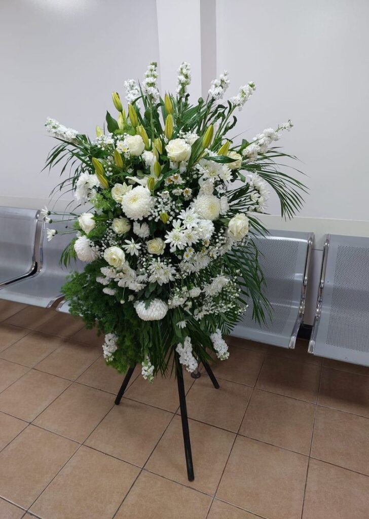 Elegant white condolence flower stand with white roses, lilies, and chrysanthemums arranged for a funeral in Dubai.